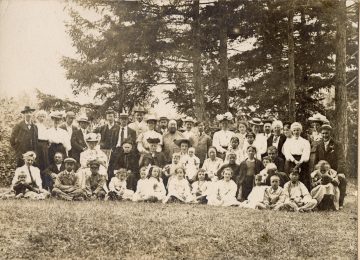 Loo Gee Wing, centre, with glasses. Surrounded by a mixed group of family and friends, including Leon J Eekman family. Text on the left reads: “This is the day when every year, friends gather together at various chosen scenic spots to eat and drink, and then go boating back at night.”