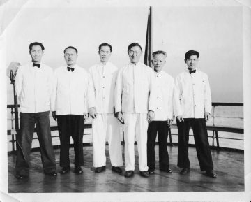 Six Chinese men in white uniforms aboard a boat.